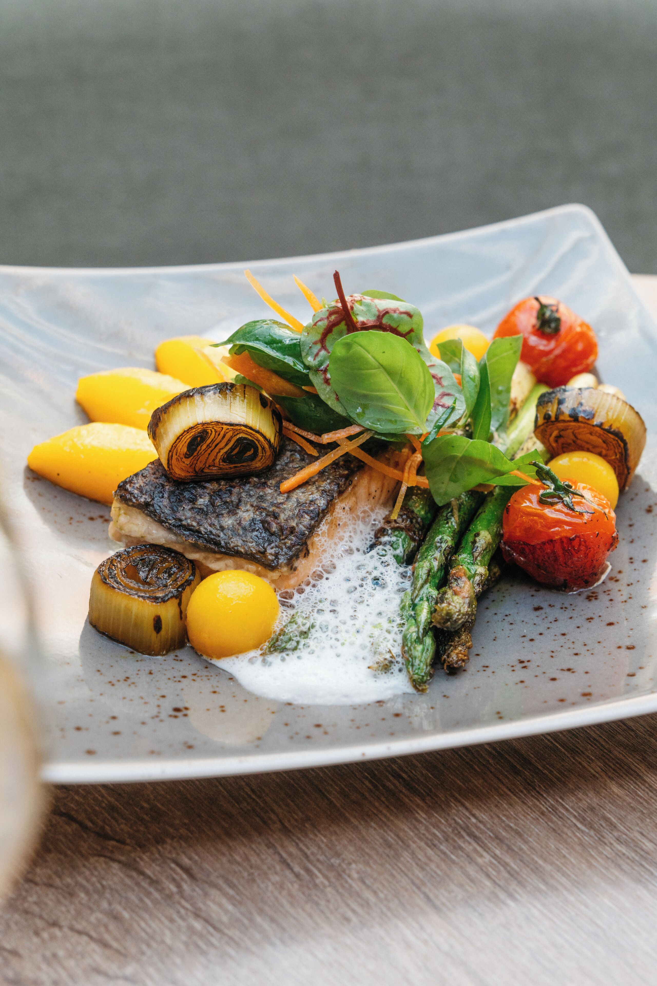 A plate of food with grilled fish, asparagus, tomatoes, and lemon slices.