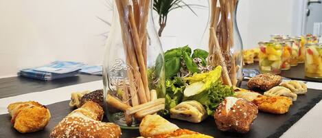 A table with various pastries and snacks, including croissants and sandwiches, in a room with artwork on the walls.