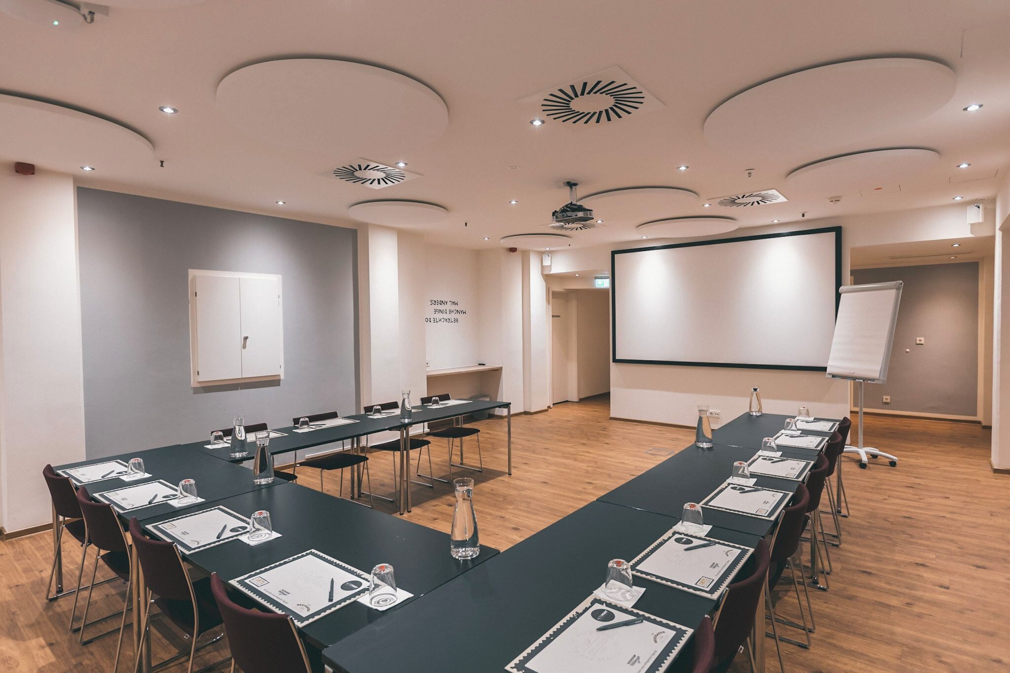 A conference room with a long table, chairs, a whiteboard, and a projector screen.