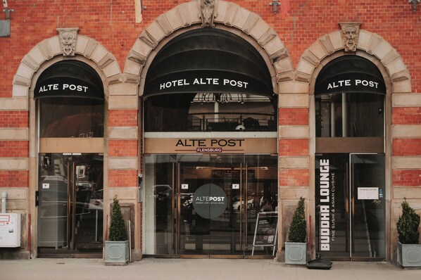 Exterior del Hotel Alte Post en Flensburg, destacando su arquitectura clásica con ventanas arqueadas y la señalización del Buddha Lounge.