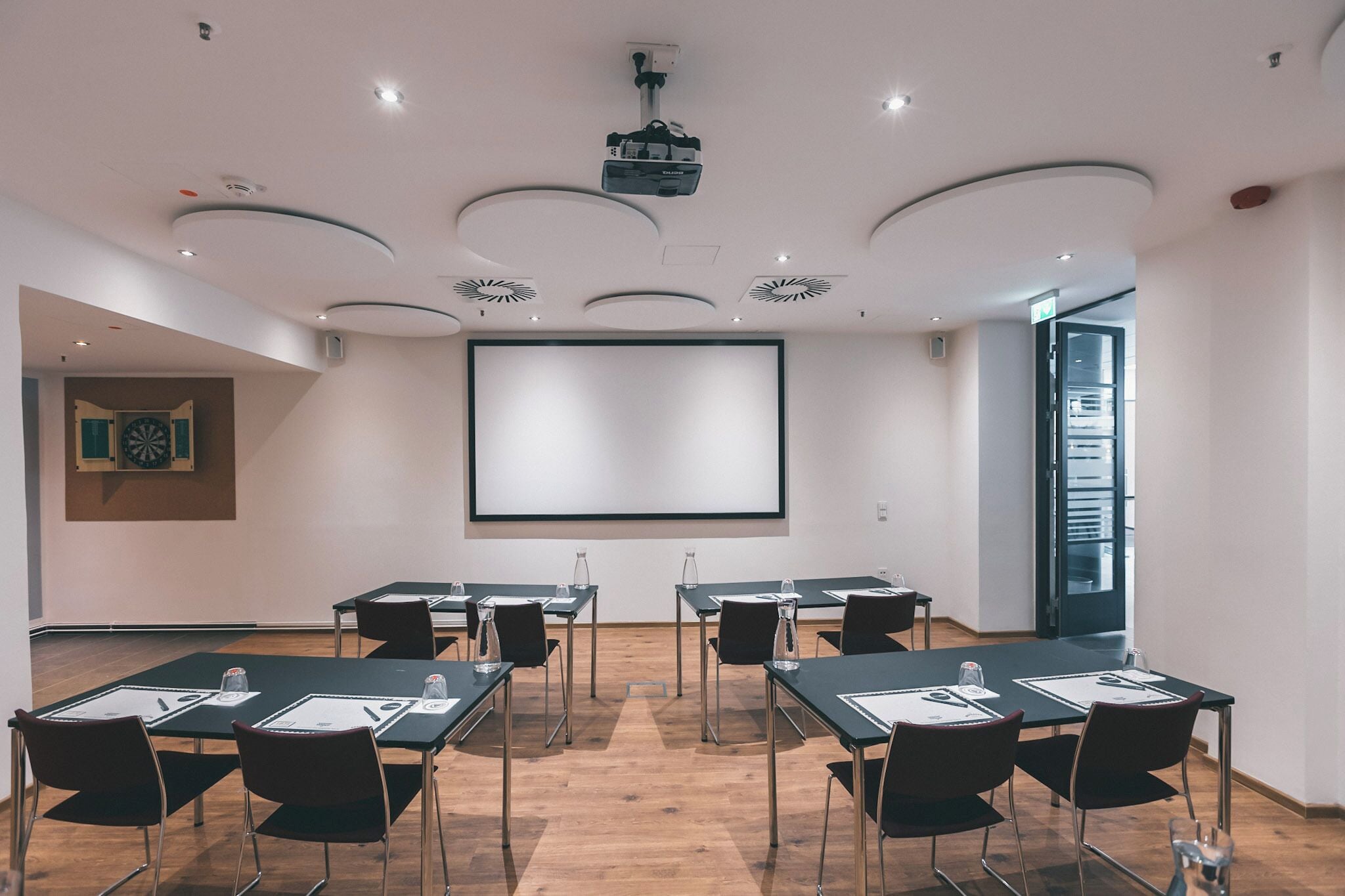 A conference room with a large screen, multiple tables with chairs, and a modern ceiling design.