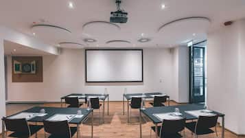 A conference room with a large screen, multiple tables with chairs, and a modern ceiling design.