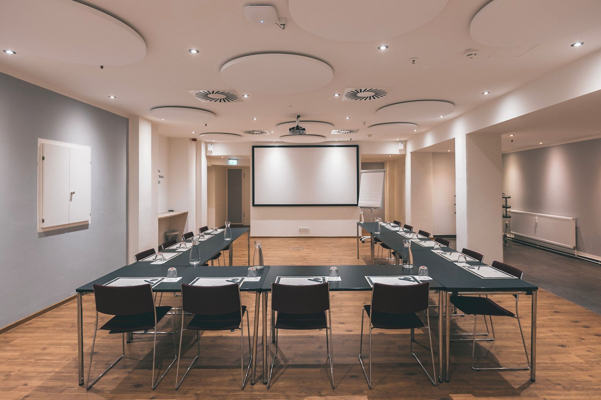 Un salón de conferencias con una larga mesa, sillas, una pantalla de proyector y una pizarra.