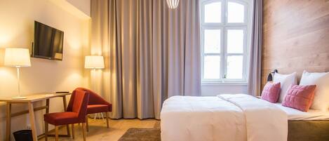 Una habitación de hotel con cama, escritorio, silla, televisor y ventana con cortinas.