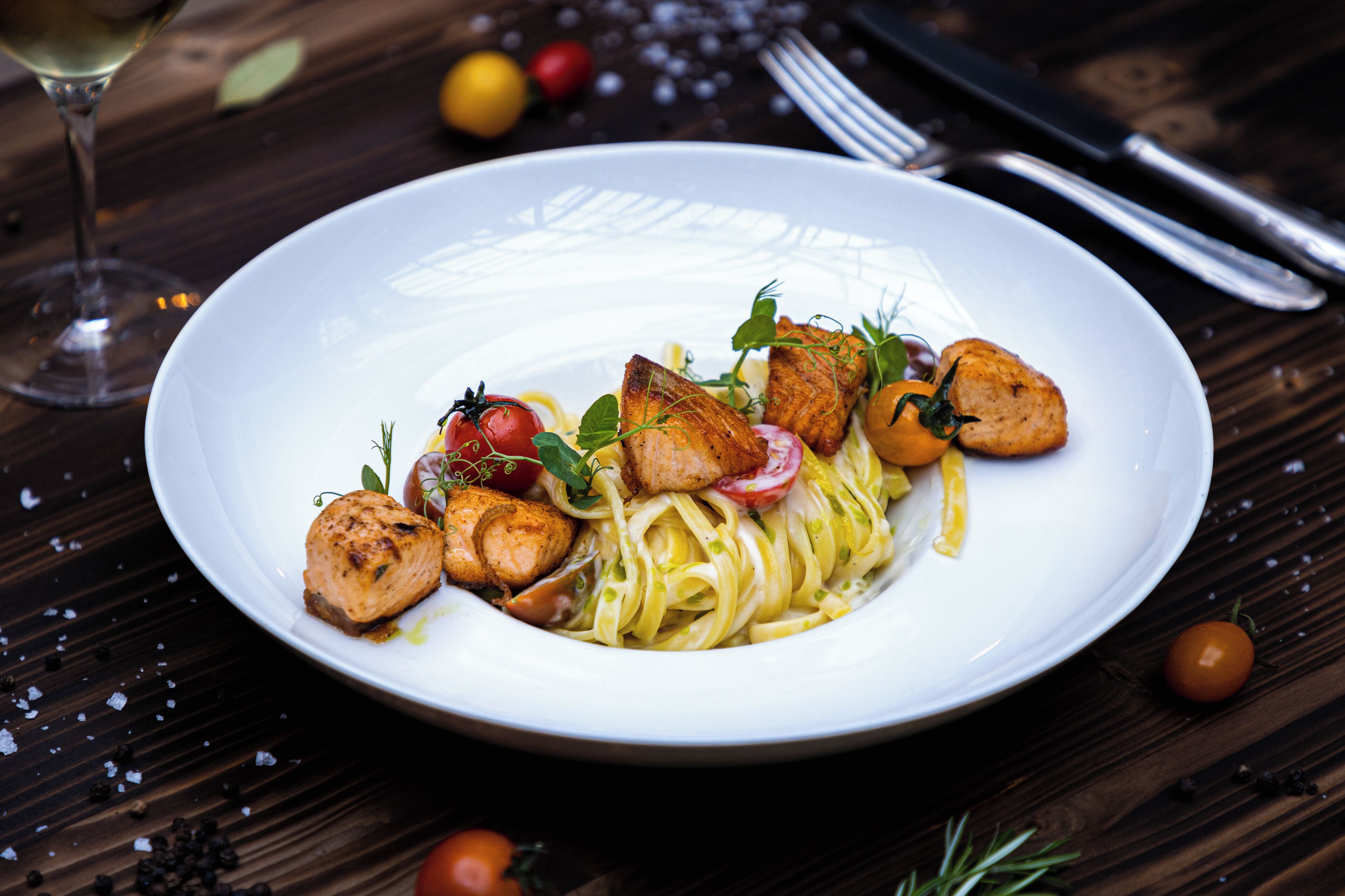 A white plate with pasta, cherry tomatoes, and grilled chicken on a wooden table.