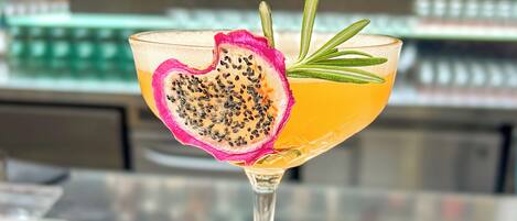 Un got de còctel amb una làmina de pitaya en forma de cor i una rameta de romaní sobre una taula blanca.