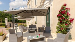 An outdoor patio with wicker furniture, a table with drinks, and a large umbrella. - Le Haut des Lys (Villandry)