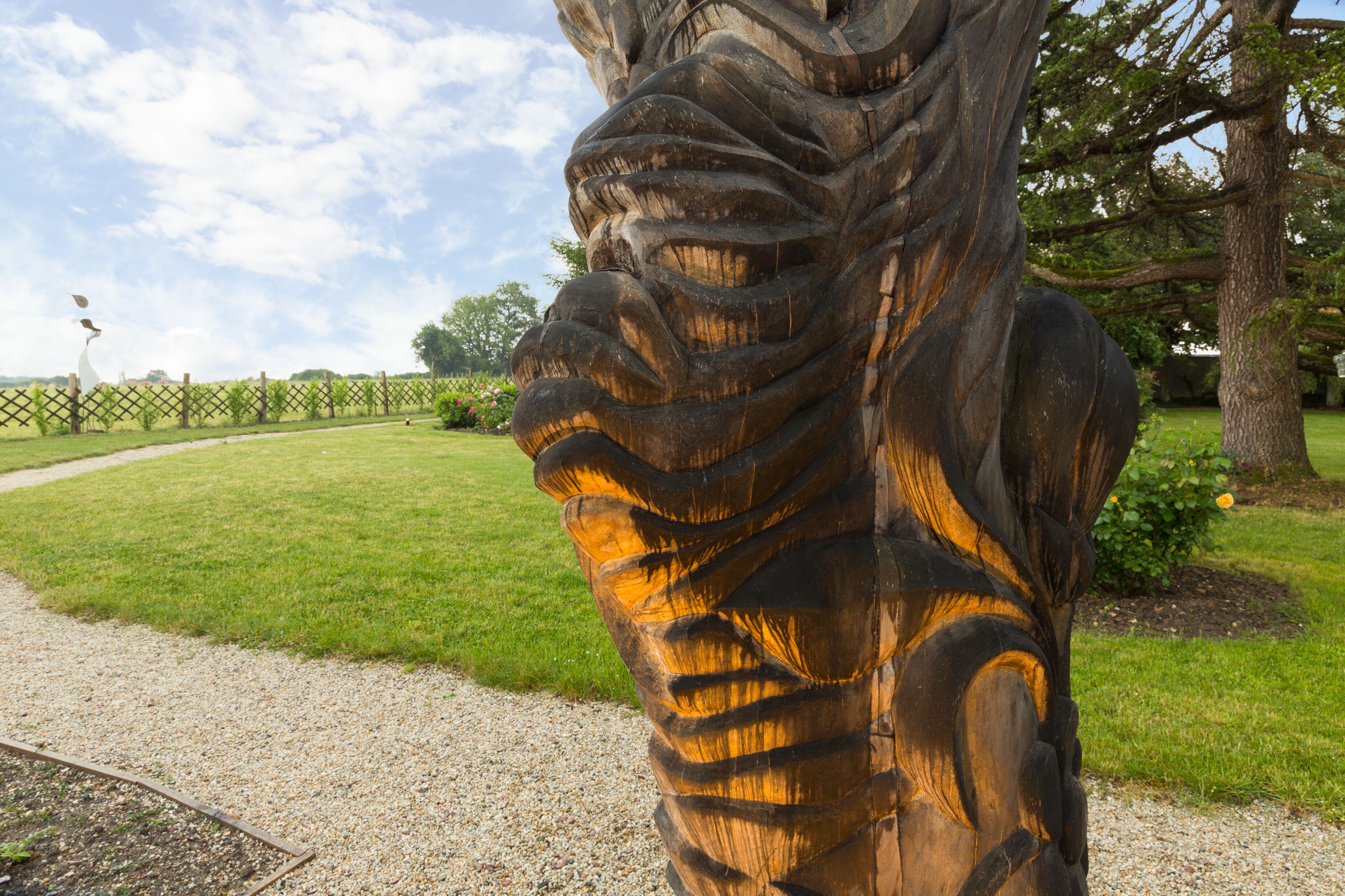 Una detallada escultura de madera en un parque con un sendero de grava y vegetación.