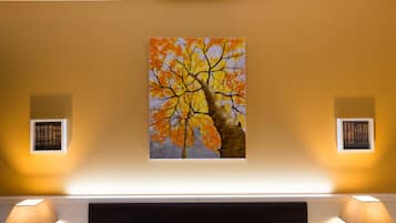 Une pièce avec un tableau représentant un arbre au mur, un lit avec une tête de lit et deux lampes fixées au mur.