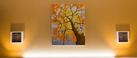 Una habitación con un cuadro de un árbol en la pared, una cama con cabecera y dos lámparas fijadas a la pared.