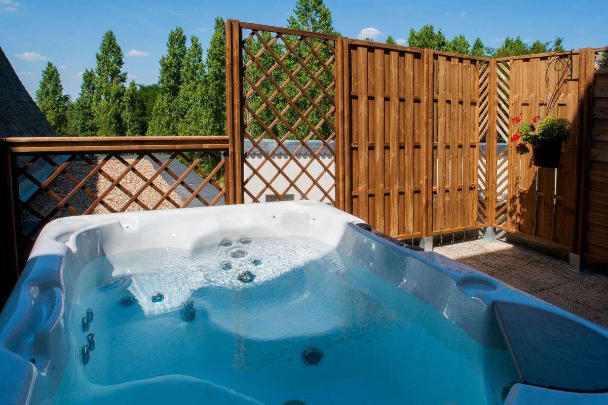 Un jacuzzi en un patio trasero con cerca de madera y una planta en maceta.