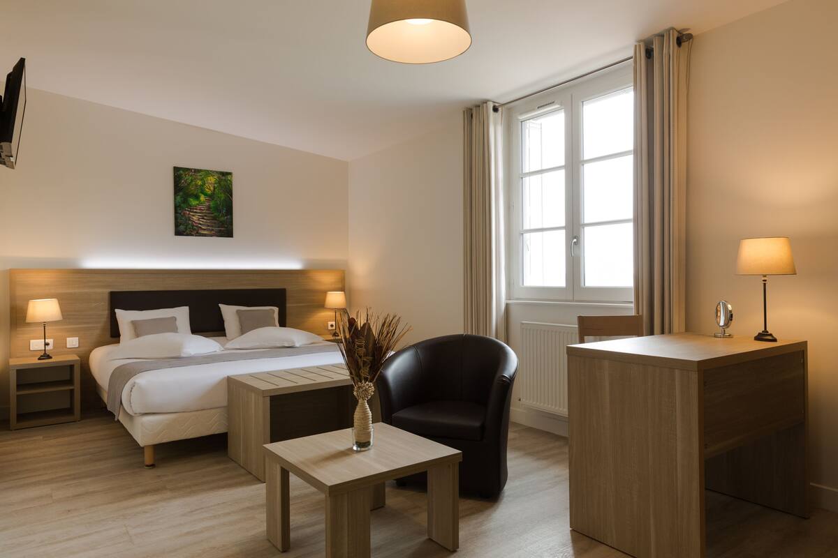Habitación de hotel con cama, mesitas de noche, escritorio, silla y ventana con cortinas.