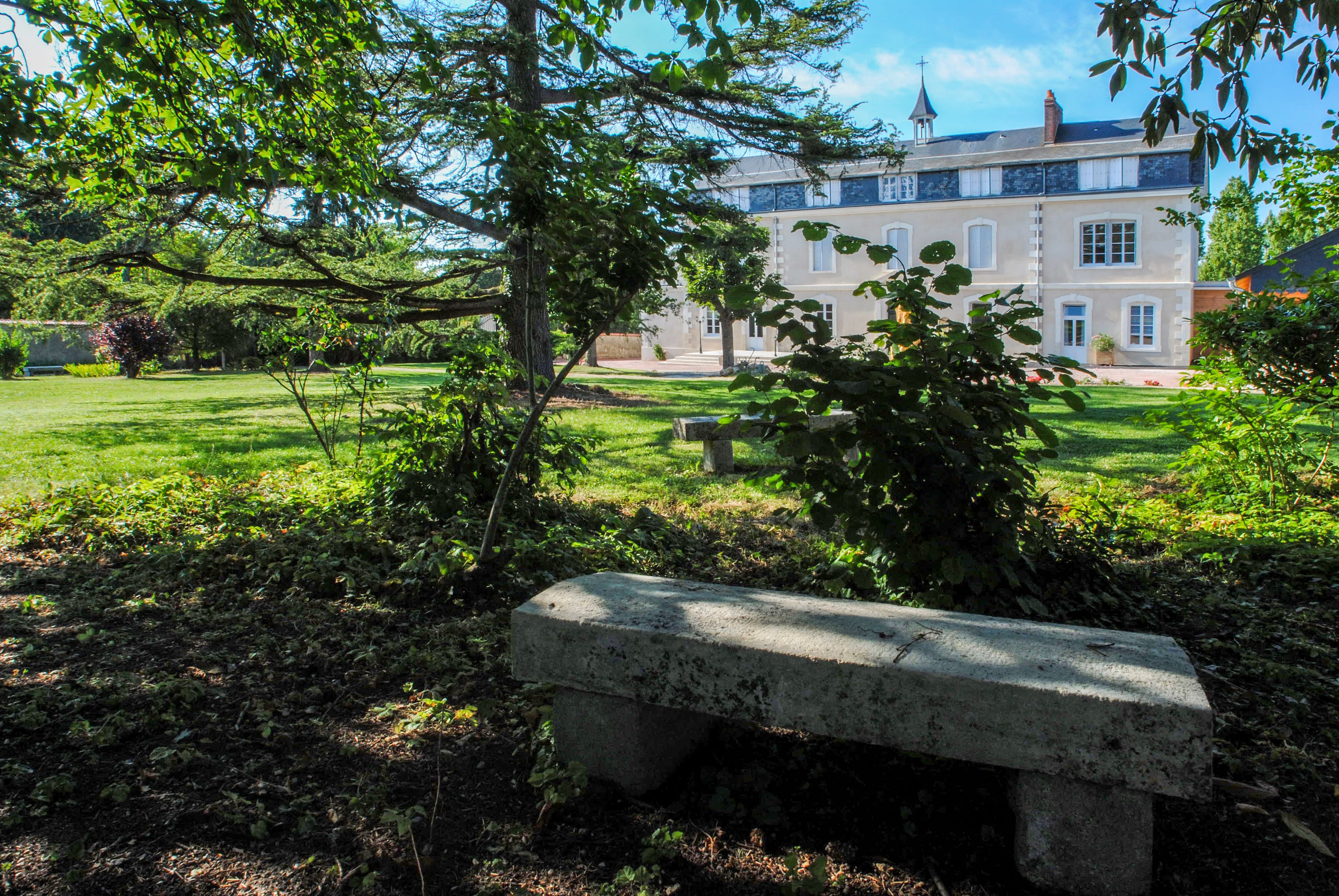 A stone bench in a lush garden with a large building in the background.