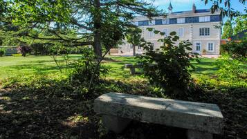 Een stenen bank in een weelderige tuin, met een groot gebouw op de achtergrond.