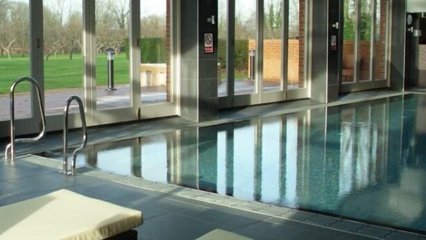 Una piscina con pareti di vetro trasparenti, una scala metallica e sedie a sdraio.