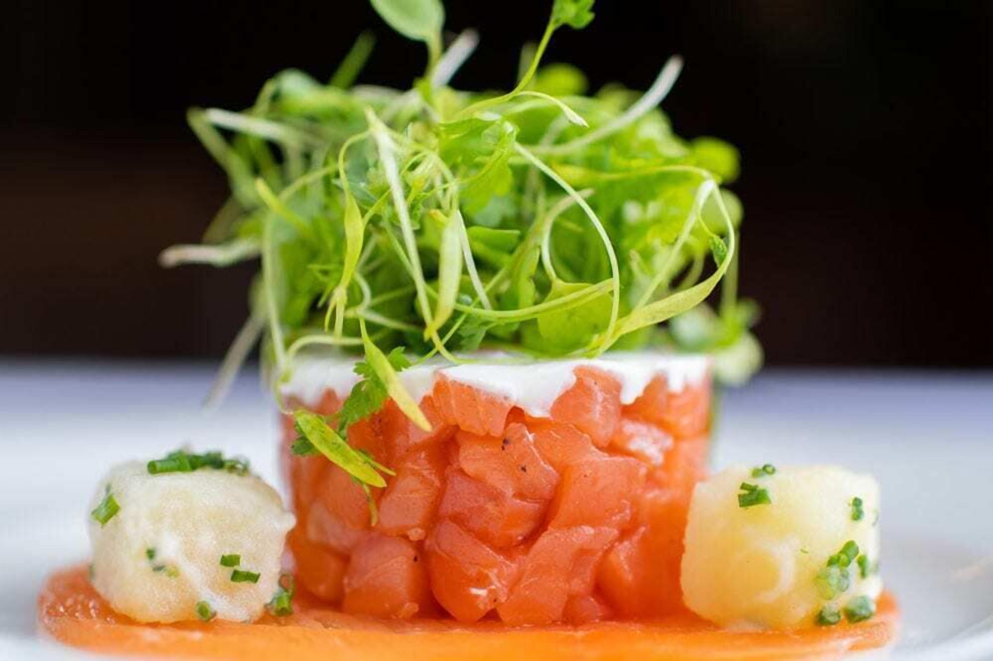 A dish with a layered structure, topped with greens, and accompanied by two spherical items and a sauce.