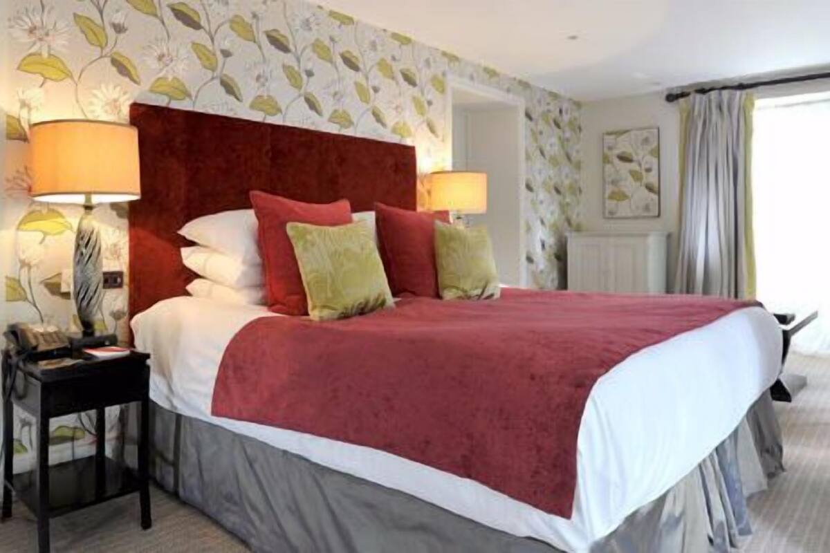 A hotel room with a large bed, two bedside lamps, a nightstand, and floral wallpaper.