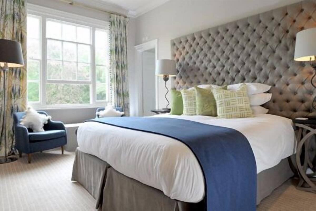 A bedroom with a large bed, tufted headboard, two bedside lamps, and a window with curtains.