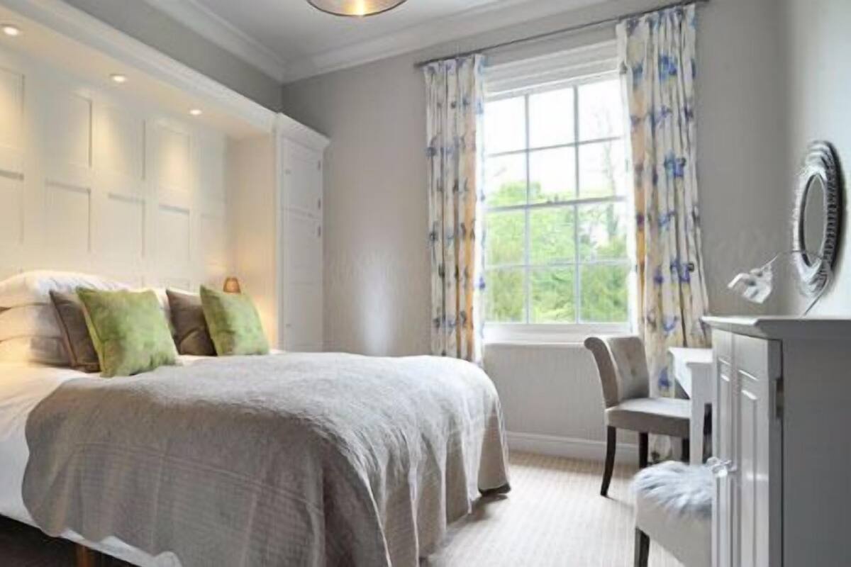 A bedroom with a bed, bedside lamps, a window with curtains, and a dresser.