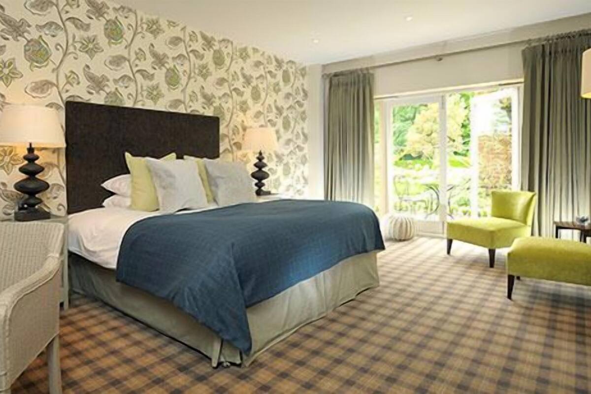 A hotel room with a large bed, a chair, a lamp, and a view of greenery outside.