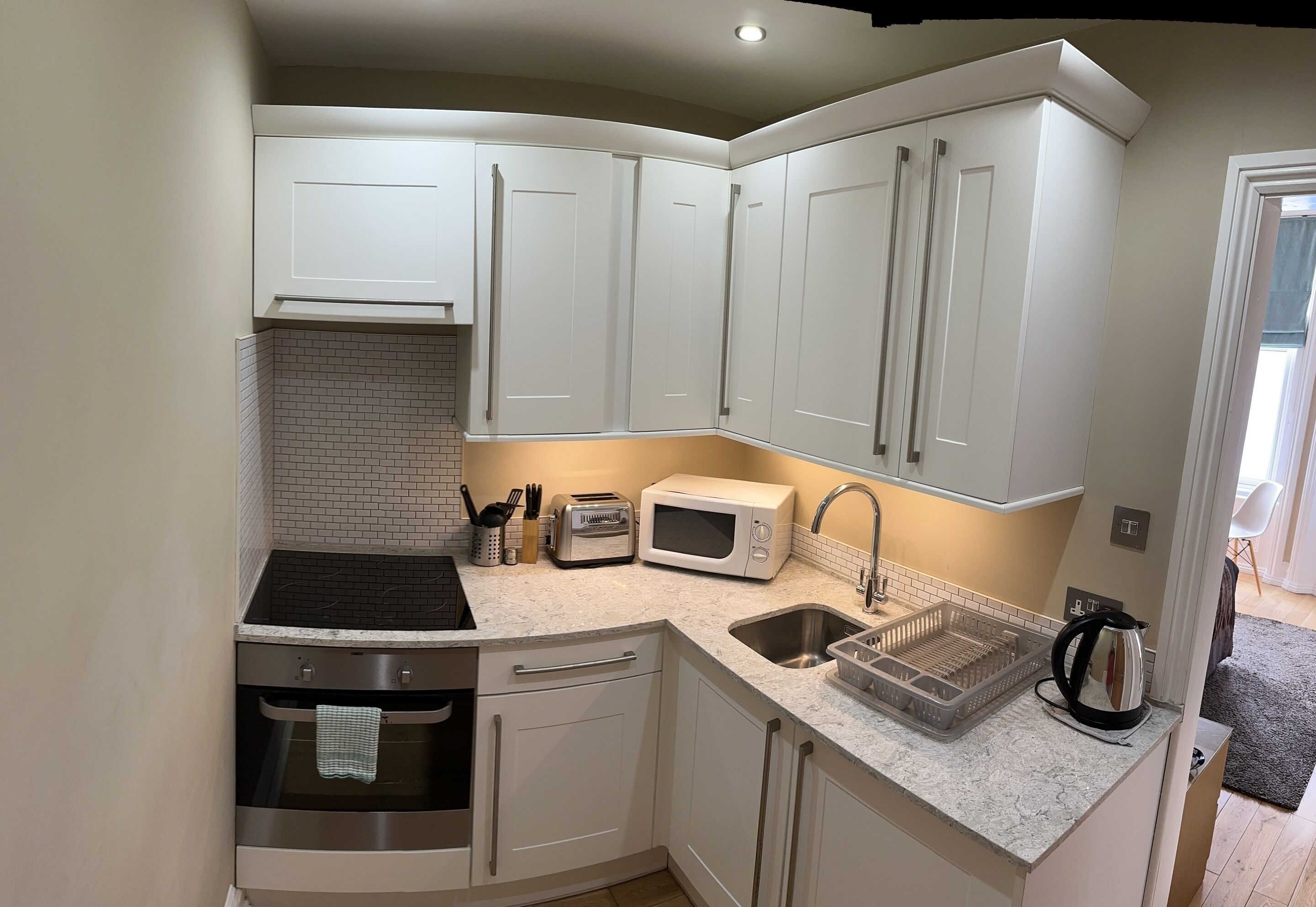 A compact kitchen with white cabinets, a microwave, toaster, sink, and a kettle.