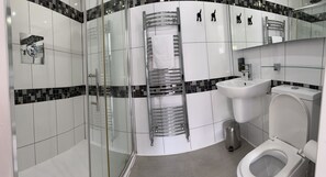A modern bathroom with a glass shower enclosure, a chrome towel rack, a white sink, and a toilet.