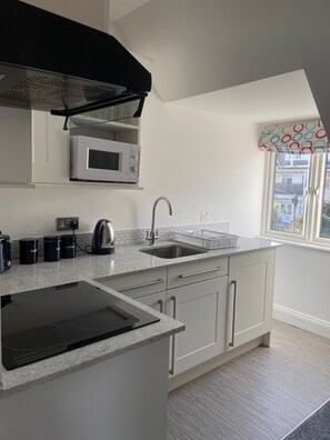 A modern kitchen with a built-in microwave, kettle, and coffee maker, a stainless steel sink, and a window with a colorful valance.