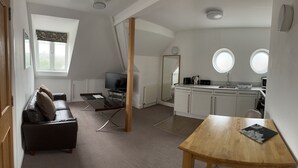 A compact living space with a sofa, a TV, a wooden table, a kitchen with a sink, and a large mirror.