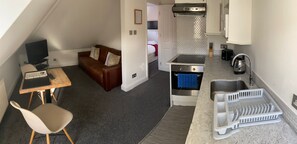 A compact living space with a kitchenette, a sofa, a dining table, and a chair.
