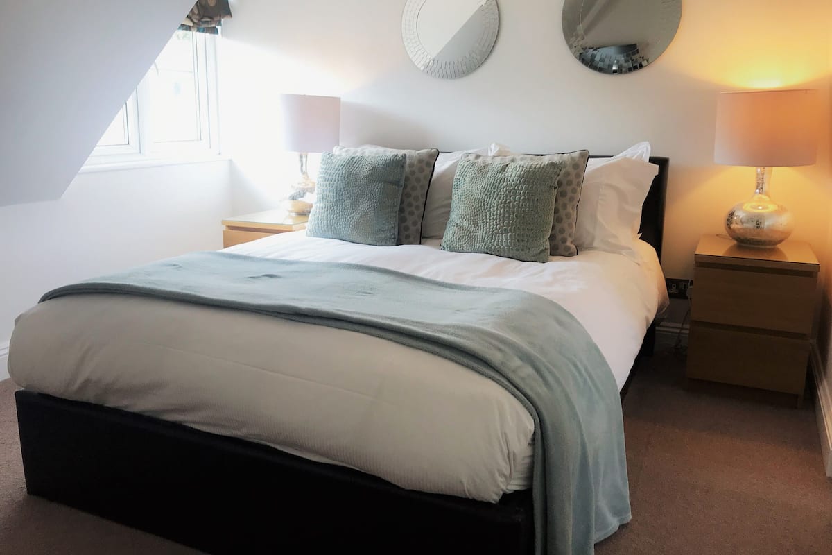 A bedroom with a bed, two bedside tables, a window, and two wall-mounted mirrors.