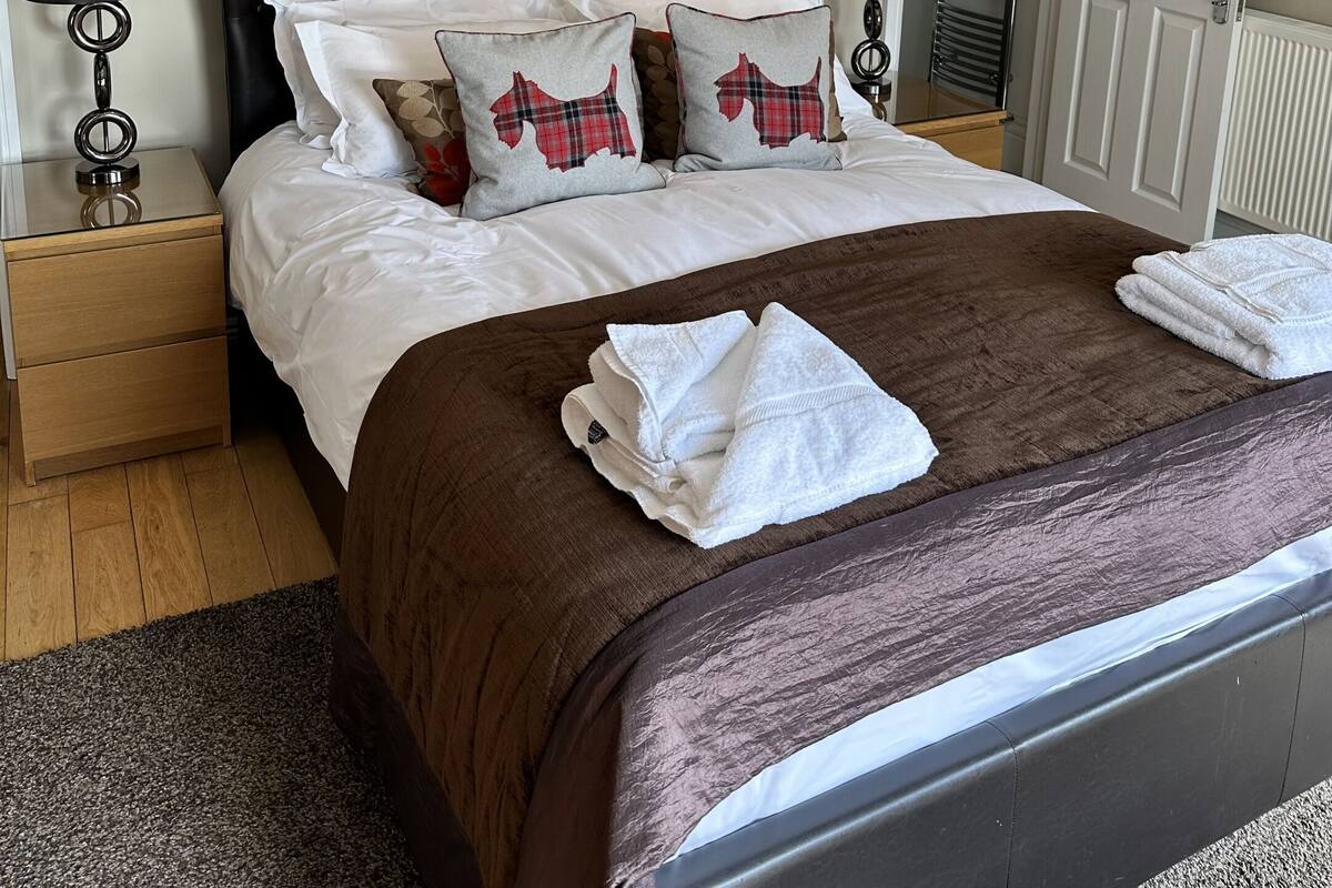 A neatly made bed with a brown bedspread, two decorative wall pieces, a black headboard, and a bedside lamp.