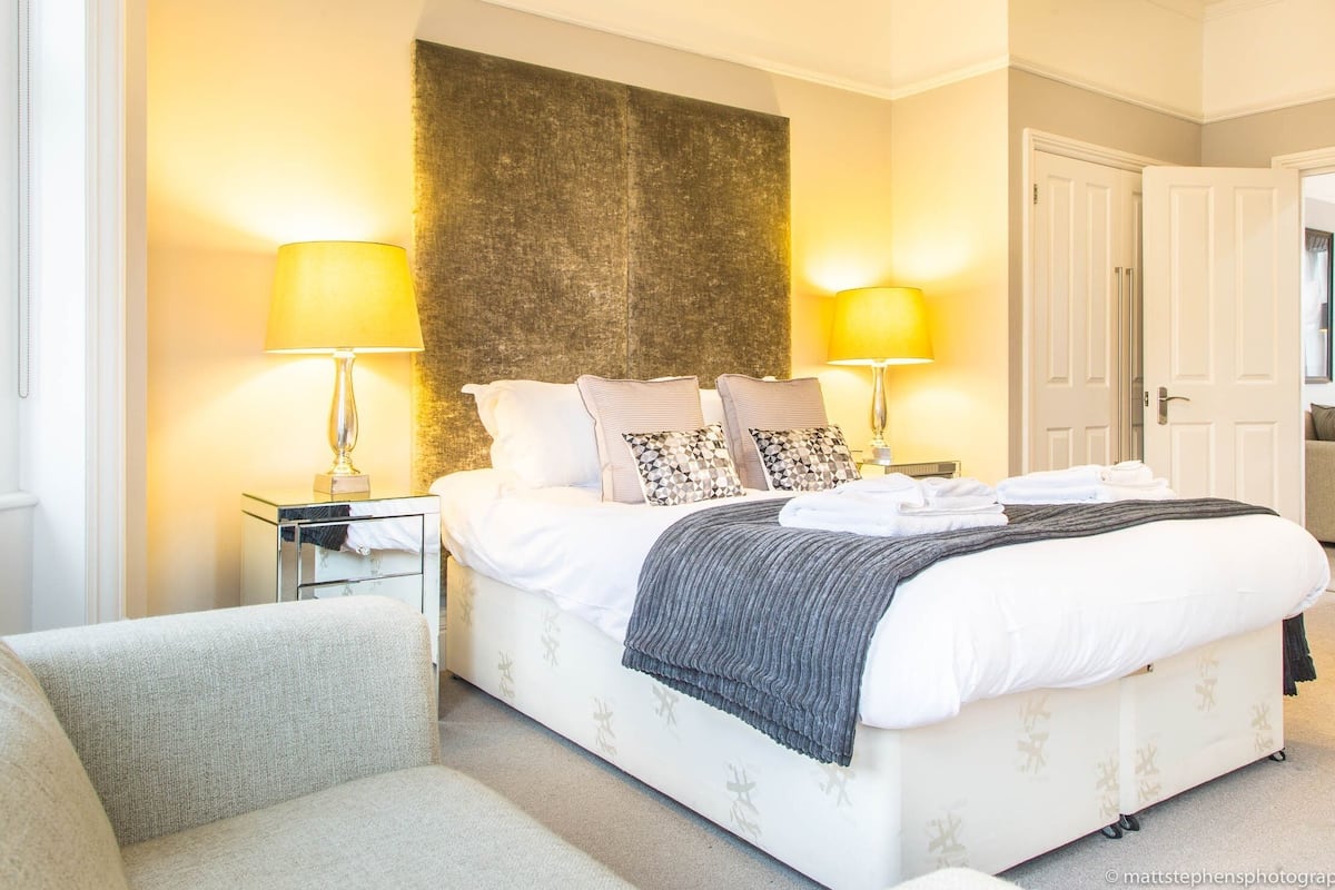 A hotel room with a large bed, two bedside lamps, a headboard, and a door.