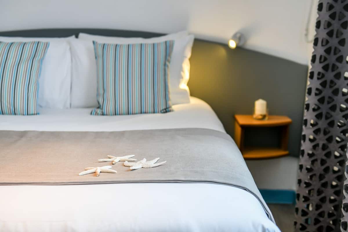 Una cama bien hecha con almohadones a rayas, una mesita de noche con una vela y una estrella de mar decorativa sobre la cama.
