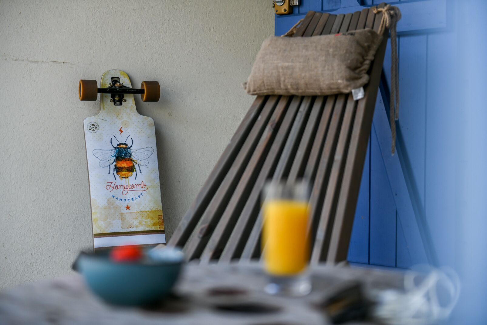 Un skateboard appuyé contre un mur, un banc en bois, un verre de jus d’orange et un bol posé sur une table.