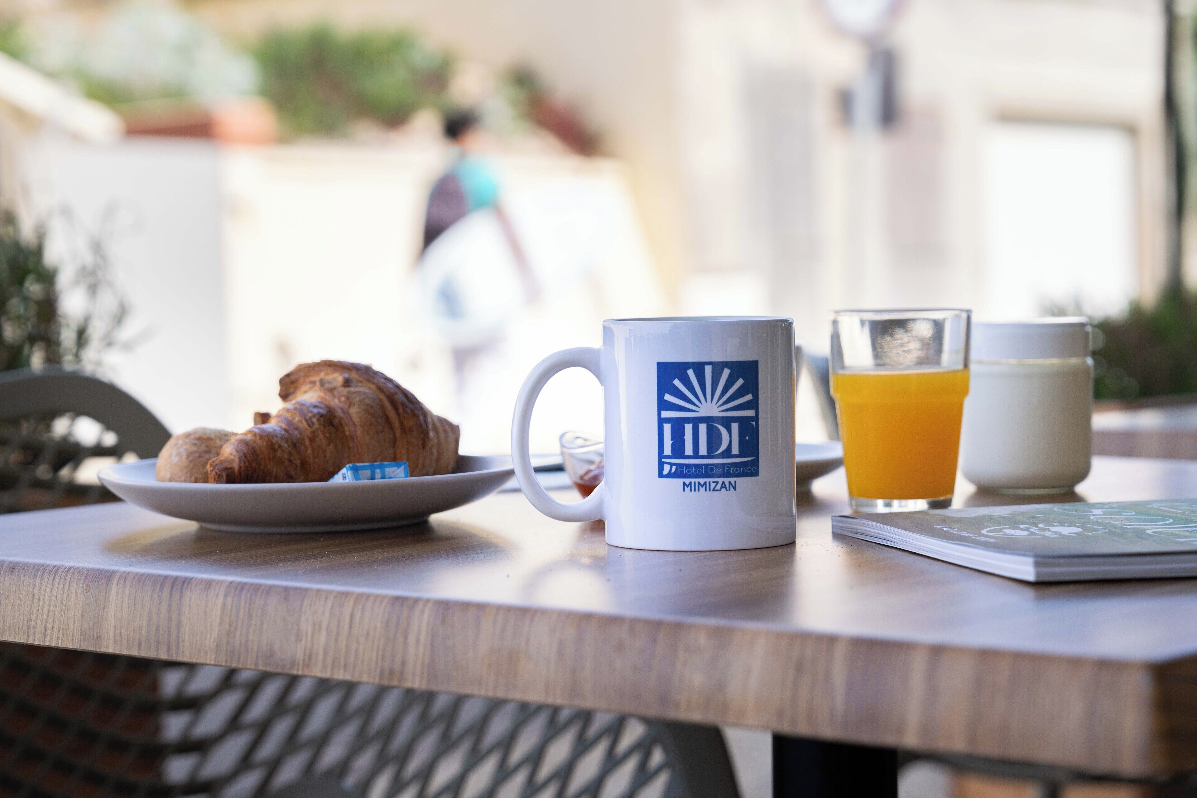 A breakfast table with a croissant, a mug, a glass of orange juice, and a milk jug.