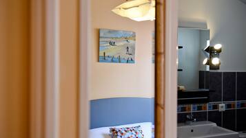 Une chambre d’hôtel avec un lit, un tableau au mur, une salle de bain avec un lavabo et un miroir, et un luminaire au-dessus du miroir.