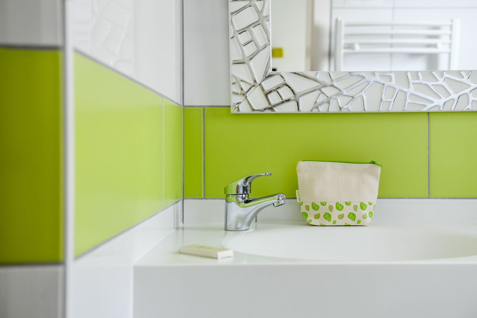 A bathroom with a white sink, a chrome faucet, and a green-tiled wall.