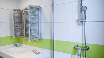A bathroom with a white sink, green-tiled walls, a shower with a handheld showerhead, and a mirror with wooden shutters.