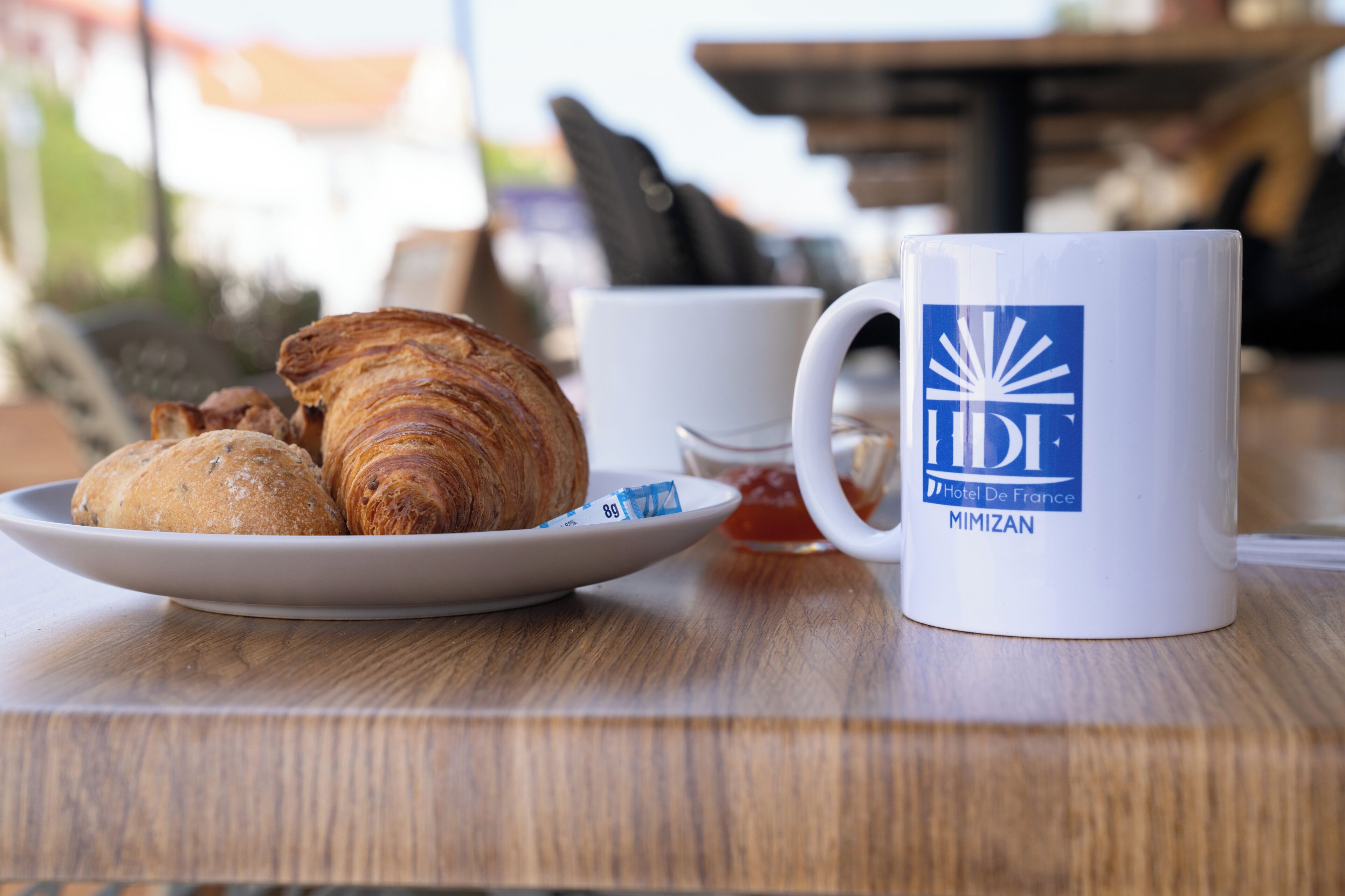 Ein Teller mit Croissants und eine Tasse mit dem Hotel-Logo auf einem Holztisch.