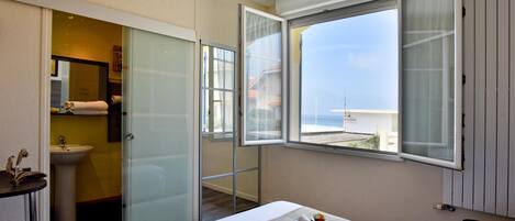 Habitación de hotel con cama, baño con lavamanos y ventana con vista al mar.