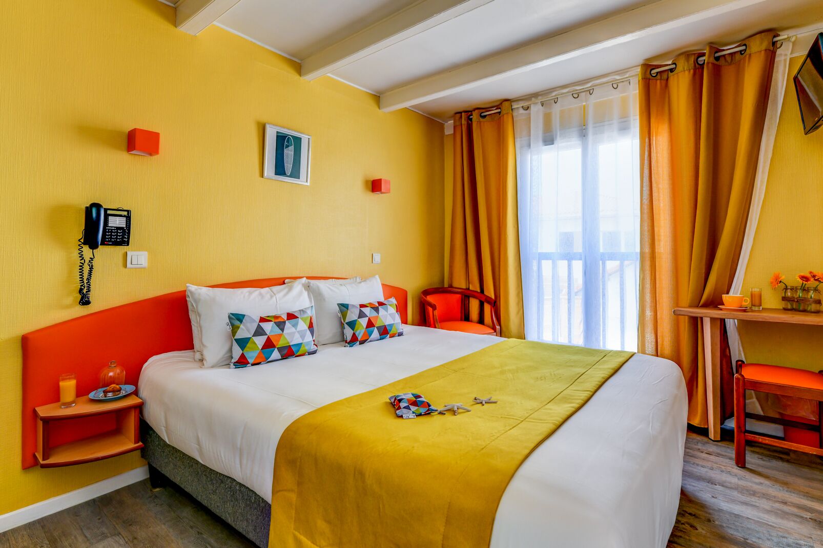 A hotel room with a bed, a bedside table, a chair, a desk, and a window with curtains.