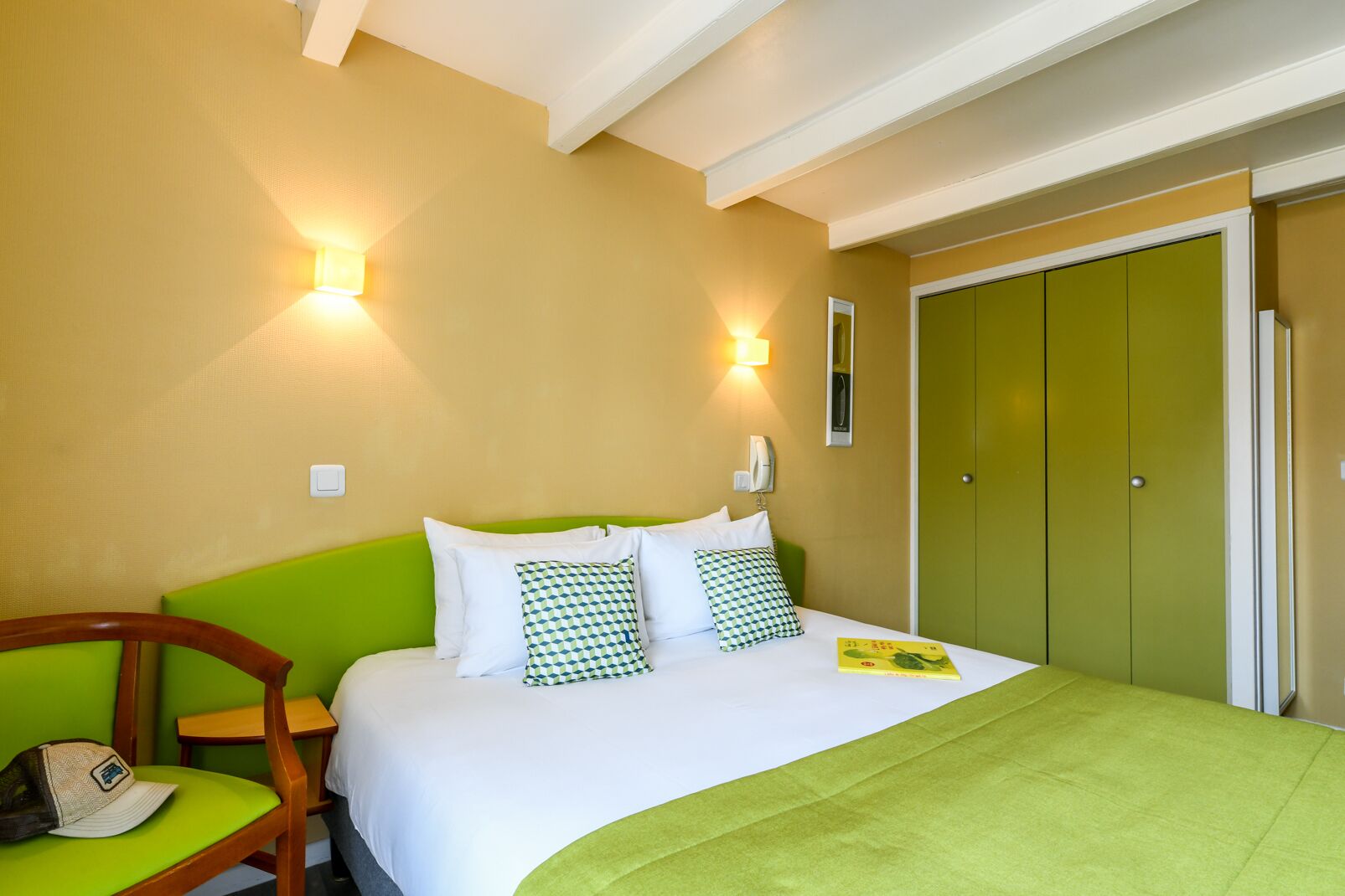 A hotel room with a bed, green walls, a wooden chair, and a green door.