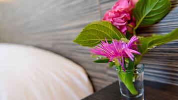 Un jarrón de cristal pequeño con una flor rosa y hojas verdes sobre una mesa de madera oscura.