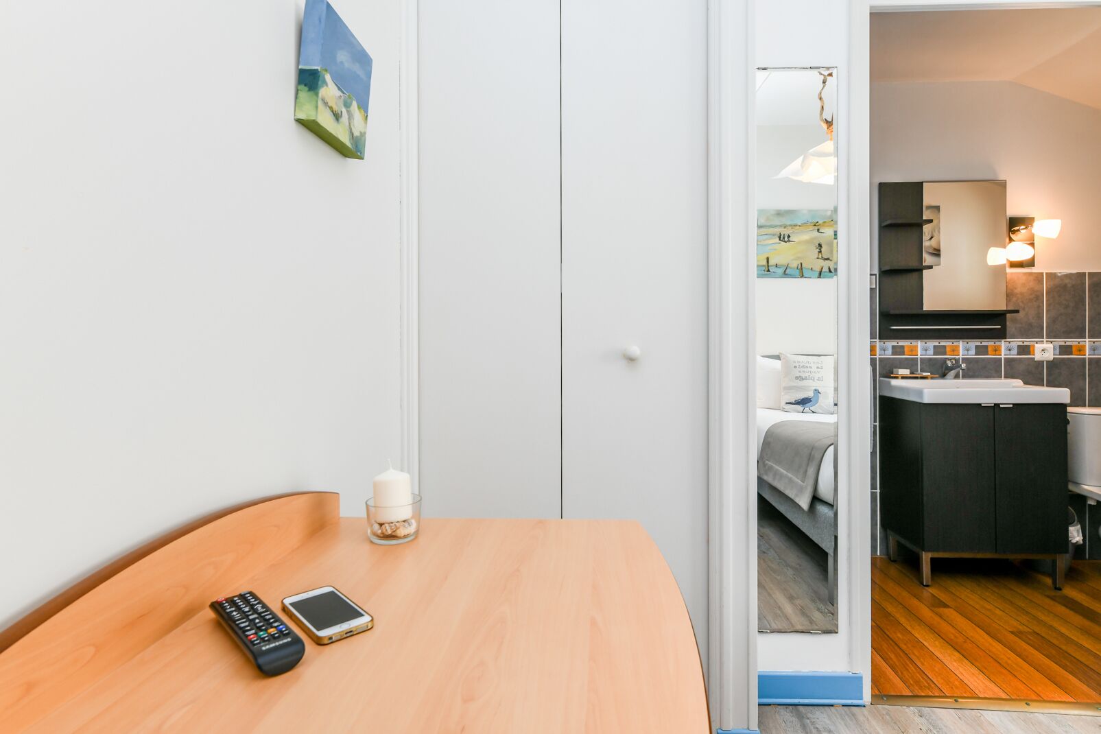 A hotel room with a wooden table, a remote control, a candle, and a bed with a view of the beach.