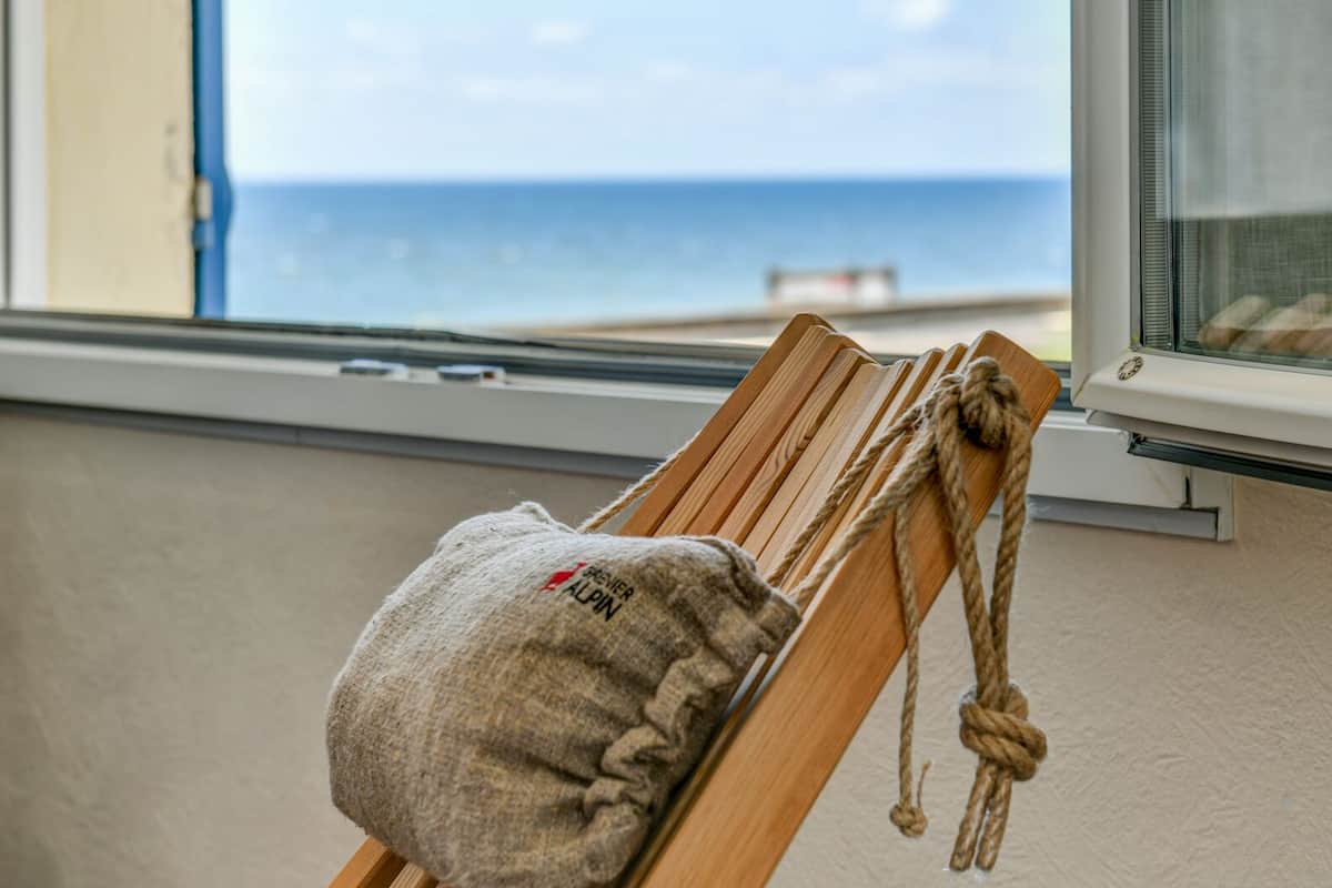 Una silla de madera con un saco de arpillera atado, ubicada junto a una ventana con vista al mar.