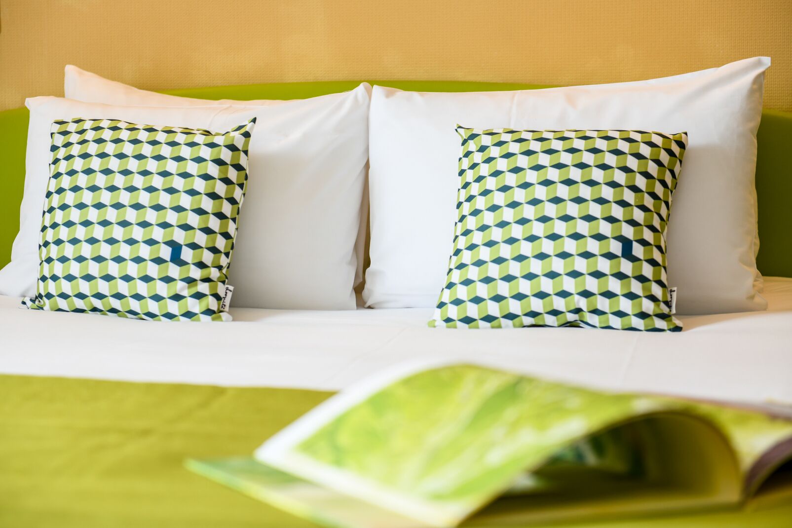 A bed with two pillows, a green bedspread, and a magazine on the bed.