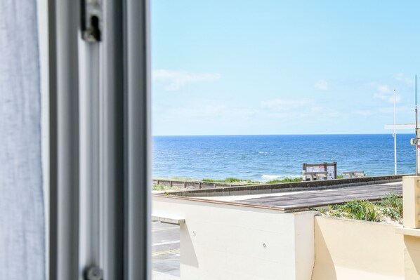 A view of the ocean through a window, with a concrete barrier and a wooden bench in the foreground. - Hôtel de France (Mimizan)