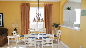 A dining area with a white table and chairs, a chandelier, and a window with curtains.
