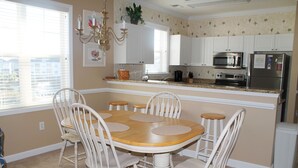 Un coin repas avec une table en bois et des chaises blanches, une cuisine avec des meubles blancs, un four à micro-ondes et un réfrigérateur.