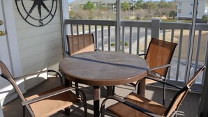 A balcony with a round table and four chairs, a compass wall decoration, and a view of a parking lot and buildings. - 434 Ironwood (North Myrtle Beach)